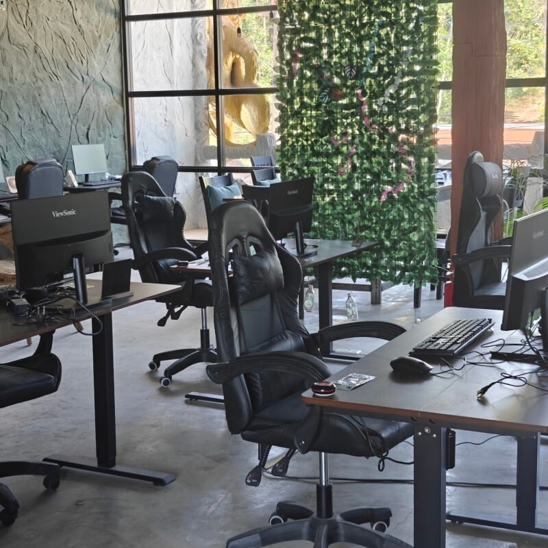 Gaming chairs and computers are set up in a room with a textured wall and a large window