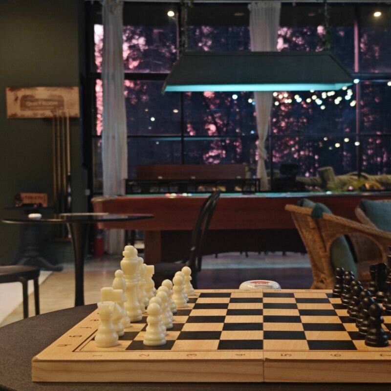 Chessboard with white and black pieces set up for a game in a dimly lit room
