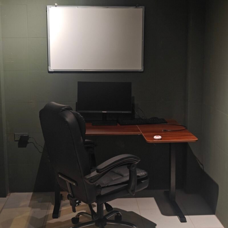 A black office chair sits in front of a desk with a computer monitor and keyboard