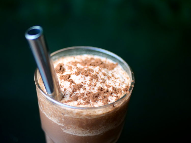 A close-up of a chocolate shake topped with cocoa powder and a metal straw